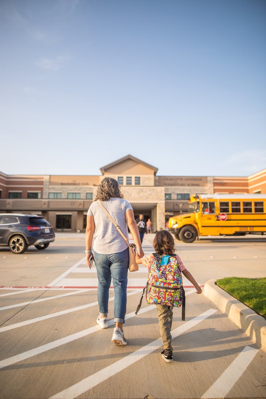 anonymous mother leading daughter to school in city