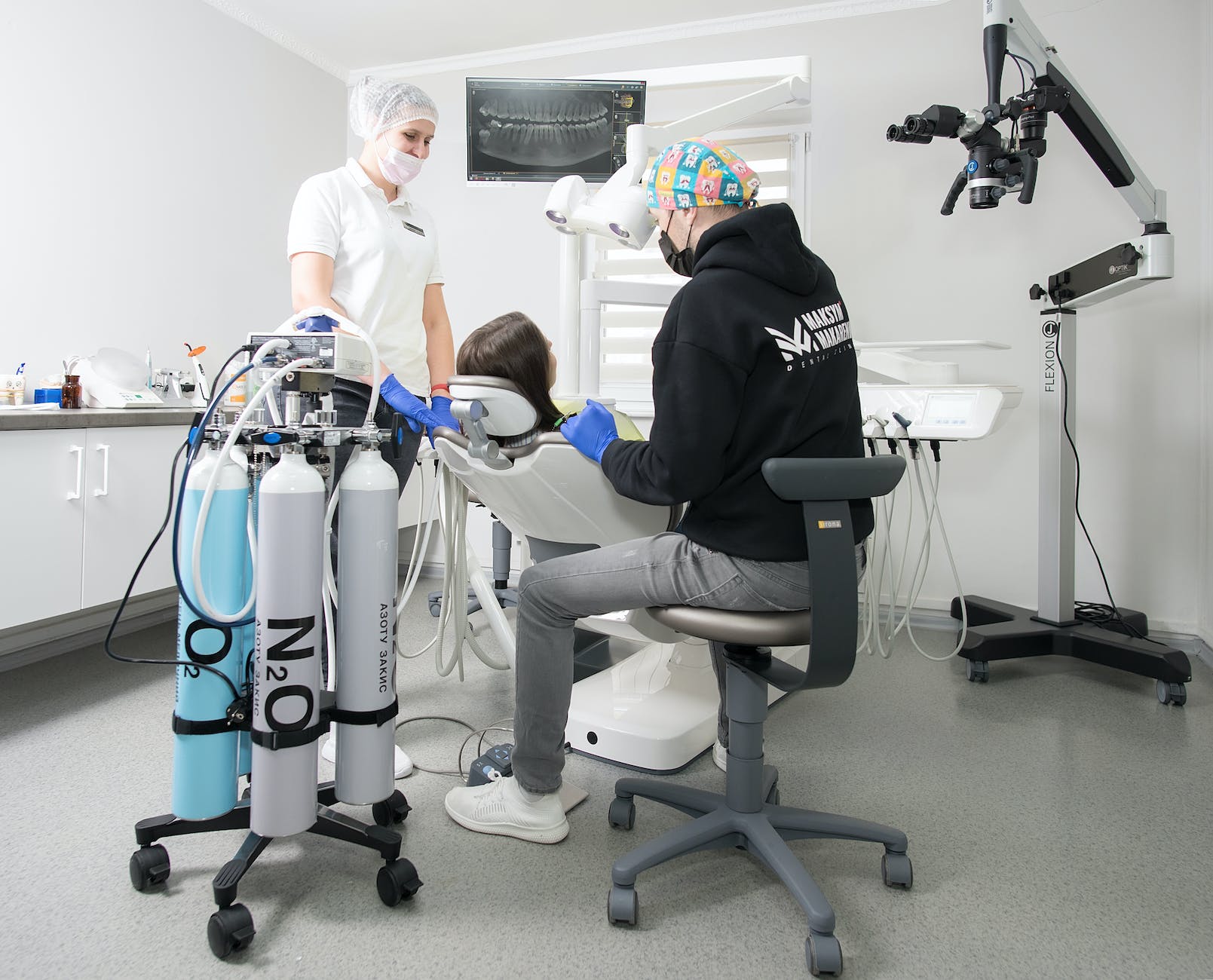 man in black hoodie sitting on gray rolling chair near patient in dental chair