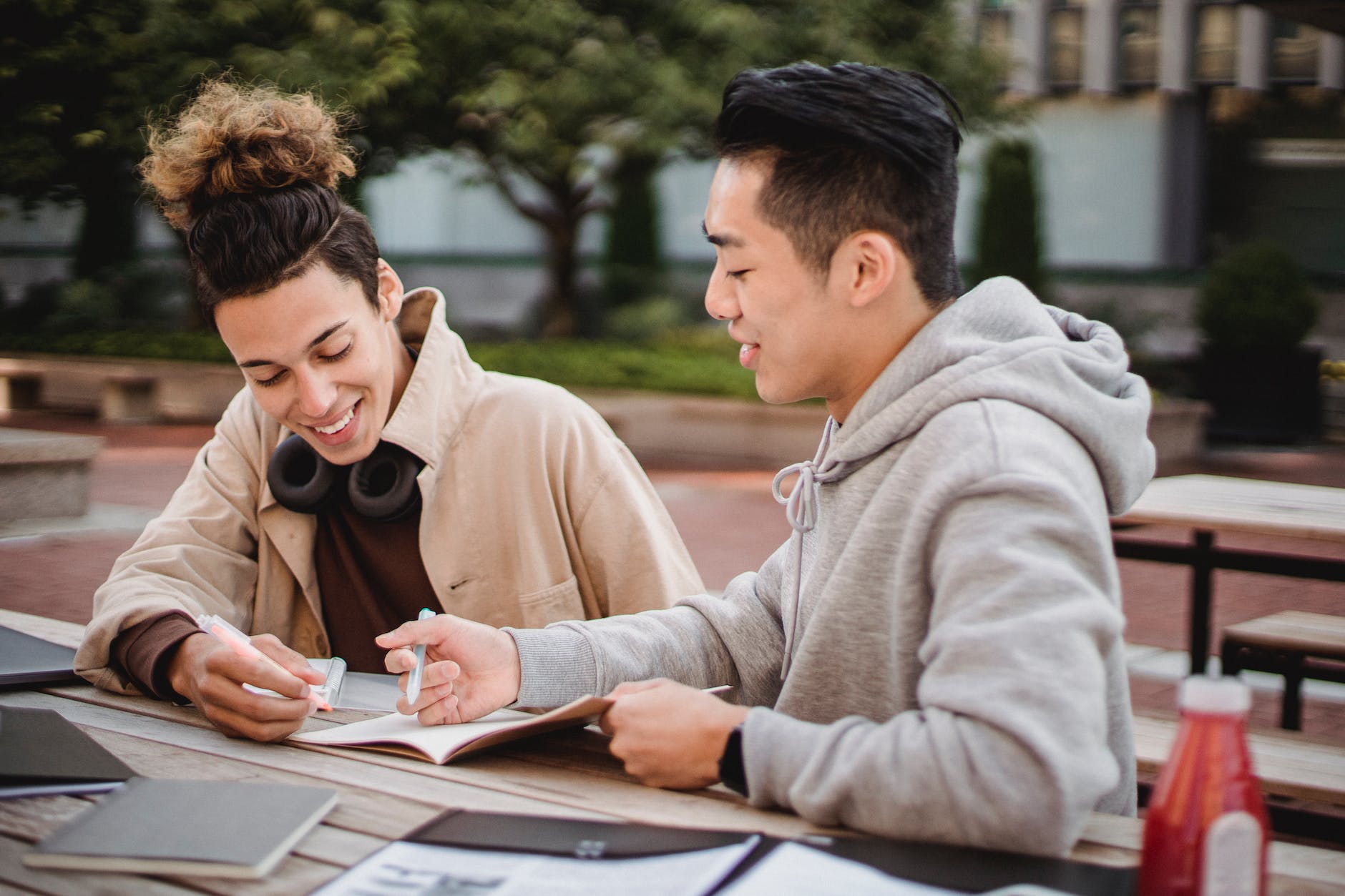 happy diverse male students working on home assignment in park